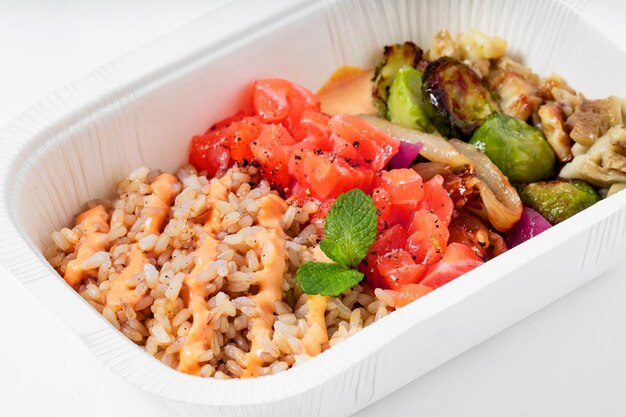 Poke avec saumon au riz brun et légumes grillés dans un contenant en plastique pour emporter