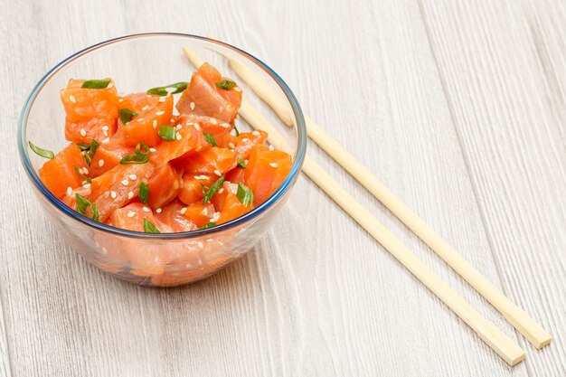 Poke de saumon hawaïen avec oignons verts et graines de sésame dans un bol en verre avec des baguettes. Vue de dessus avec espace de copie. Fruits de mer biologiques