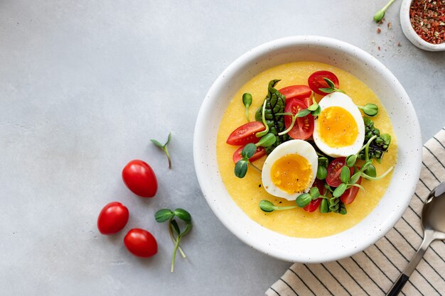 polenta ou bouillie de maïs servie avec des légumes frais et des œufs bol déjeuner sain et équilibré