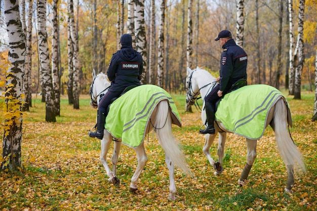 Police montée dans le parc de la ville d'automne, vue arrière. Deux policiers russes patrouillent à cheval dans le parc. Inscription POLICE au dos.