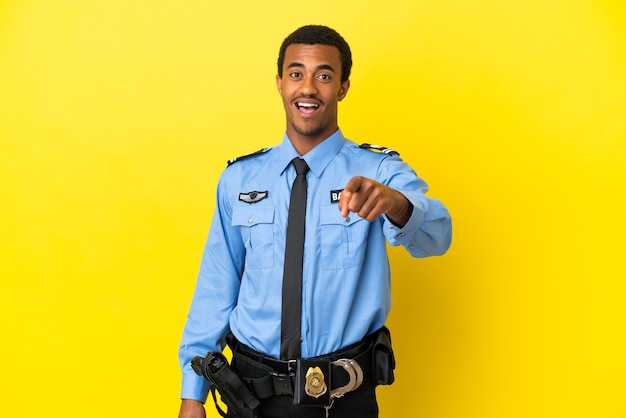 Un policier afro-américain sur un mur jaune isolé surpris et pointant vers l'avant