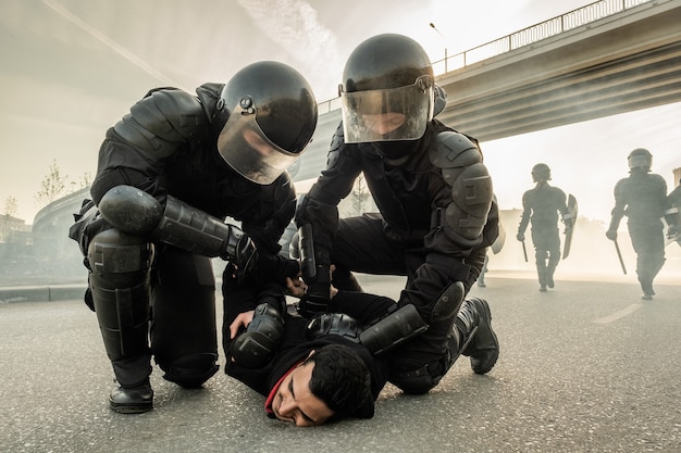 Un policier anti-émeute fort dans des casques tordant les bras d'un manifestant derrière son dos tout en l'arrêtant dans la rue