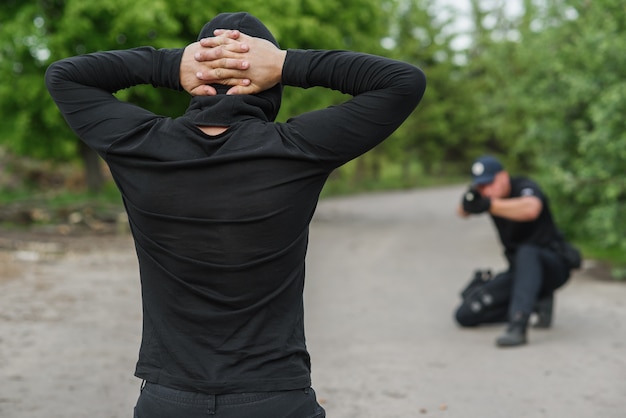 Photo le policier vise un terroriste. le délinquant est à genoux, les mains repliées sur la tête.