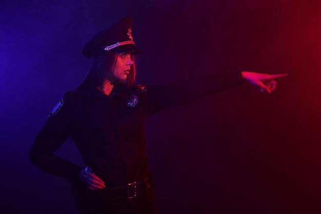 Une policière rousse pose pour la caméra sur un fond noir avec du rouge et du bleu...