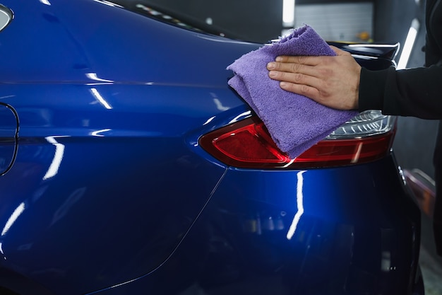 Polissage de voiture. Chiffon bleu dans les mains. Détaillant de voiture dans le garage.