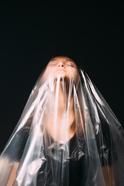 Pollution plastique. Problème d'écologie. Sauvez la nature. Portrait d'art d'une femme fatiguée aux yeux fermés essayant de respirer dans un sac en film de polyéthylène transparent isolé sur fond d'espace de copie noire.