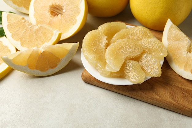 Pomelo mûr et plaque avec tranches de pomelo sur fond texturé blanc