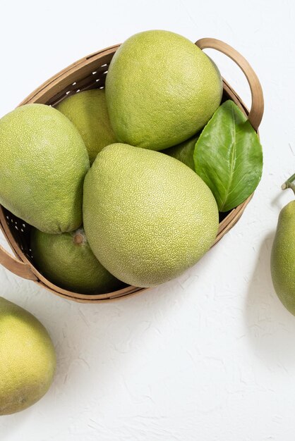 Photo pomelo pommelo frais shaddock de pamplemousse sur fond de ciment blanc dans un panier de bambou fruit de saison d'automne vue supérieure sur une table plate