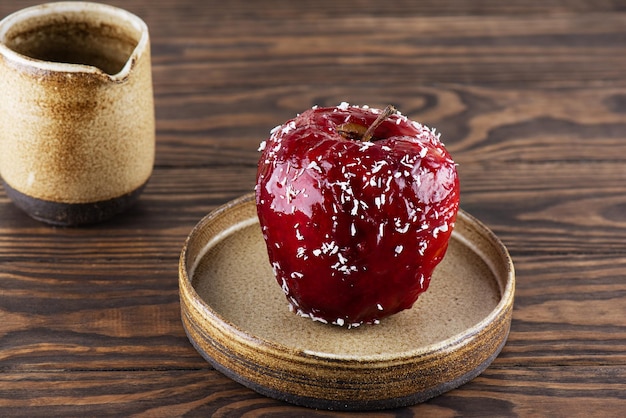 Pomme au four avec noix et miel en glaçure rouge avec flocons de noix de coco sur une table en bois.