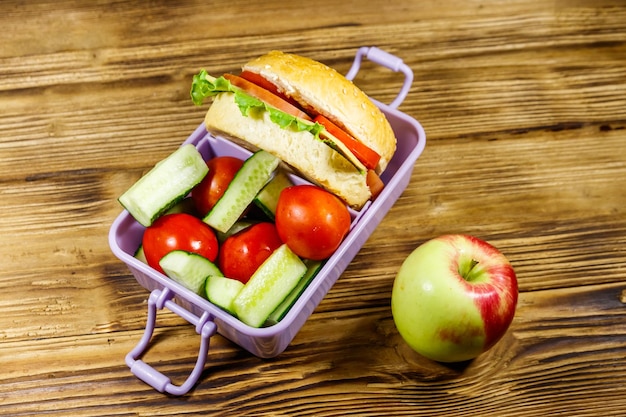 Pomme et boîte à lunch avec des hamburgers et des légumes frais sur une table en bois