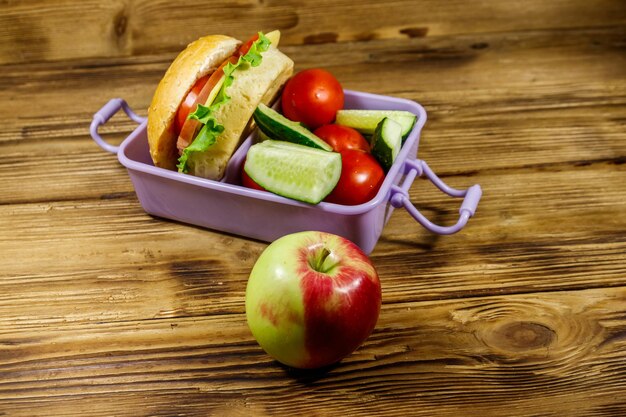 Pomme et boîte à lunch avec des hamburgers et des légumes frais sur une table en bois