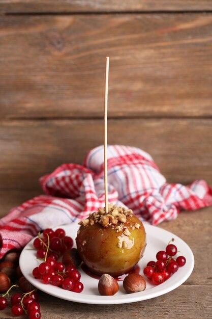 Pomme caramel sucré sur bâton avec baies, sur table en bois