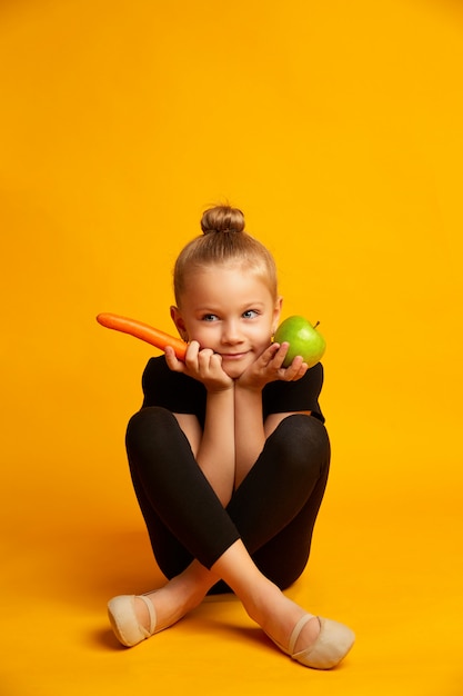 Une pomme, une carotte et une fille sportive sur fond jaune. Suivre un régime et manger sainement