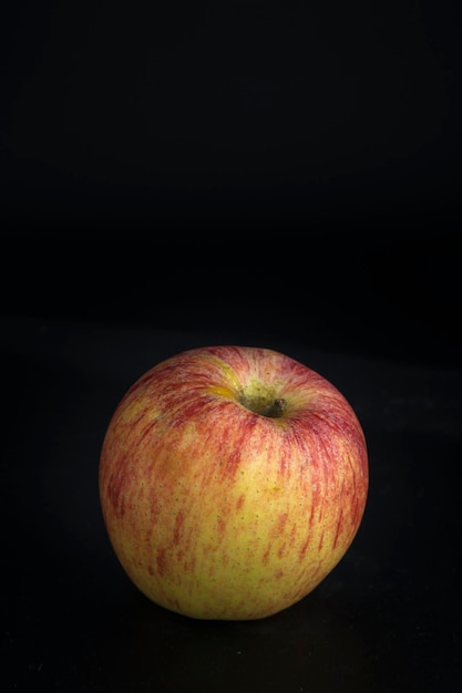 Photo pomme sur fond noir vue d'une pomme rouge et jaune placée contre l'obscurité maximale