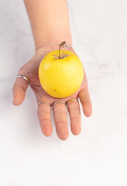 Pomme jaune en mains sur un mur de marbre