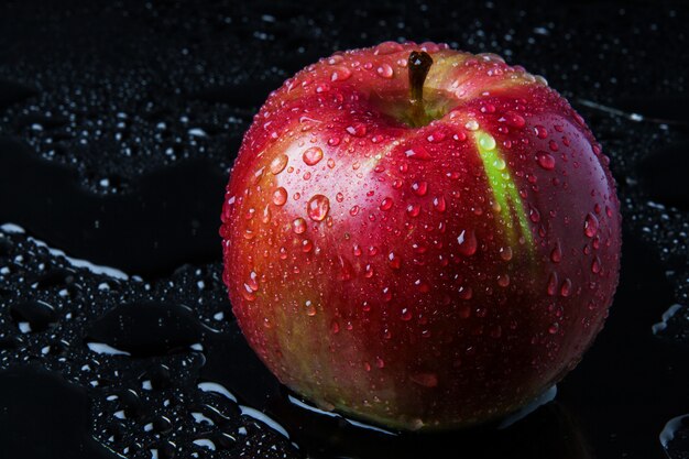 Pomme à rayures rouges avec des gouttes de pluie, sur le verre noir humide