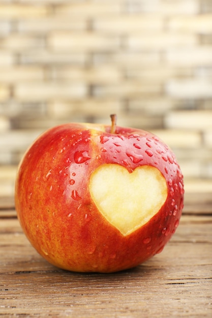 Pomme rouge avec coeur sur table en bois, gros plan