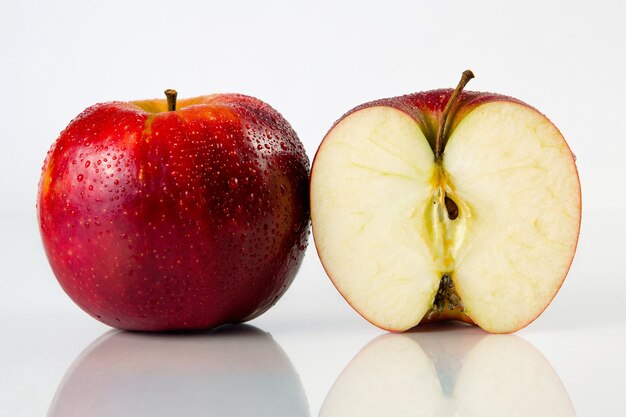 Pomme rouge et demi avec des gouttes d'eau sur fond blanc avec réflexion