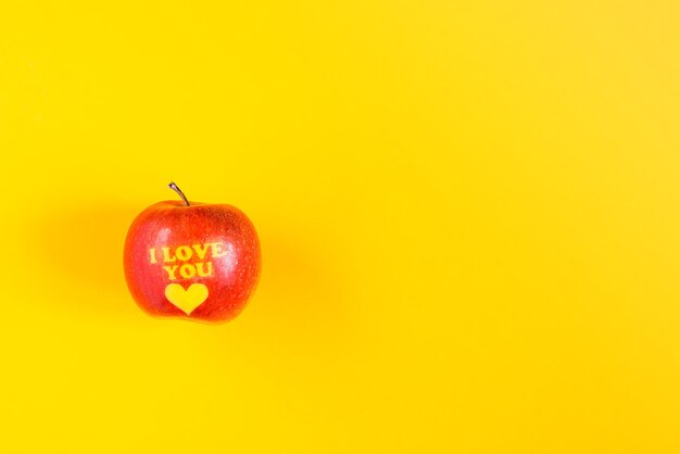 Pomme rouge fraîche avec des mots je t'aime et coeur sur fond jaune vif.