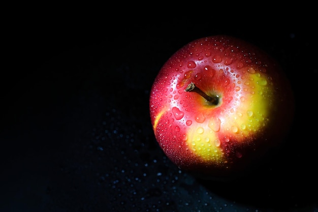 Pomme rouge avec des gouttes d'eau sur un gros plan de fond noir