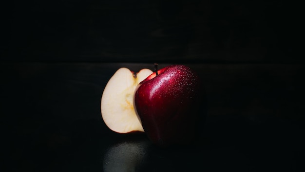 Une pomme rouge et une moitié de pomme sur fond noir.