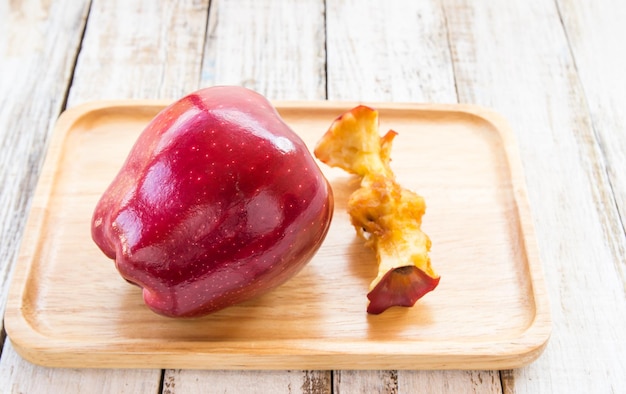 Pomme rouge et trognon de pomme dans une assiette en bois sur un fond en bois blanc