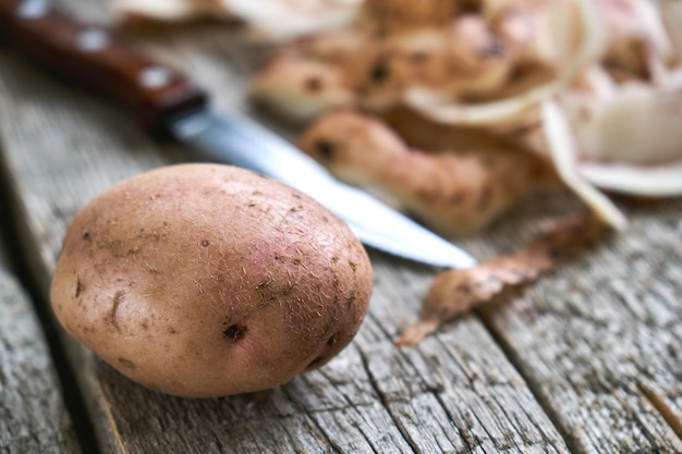 Pomme de terre non pelée avec épluchure de pomme de terre et un couteau sur les planches de bois