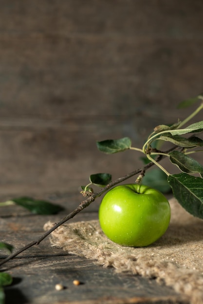 Pomme verte avec des feuilles sur toile de jute sur des planches de bois