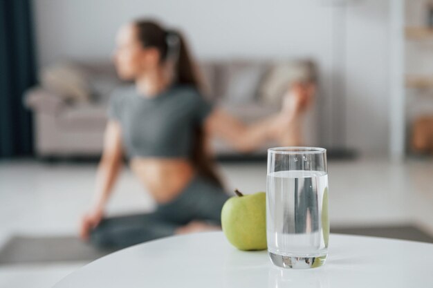 Pomme verte et verre d'eau est sur la table Jeune femme avec un type de corps mince et dans des vêtements de yoga est à la maison