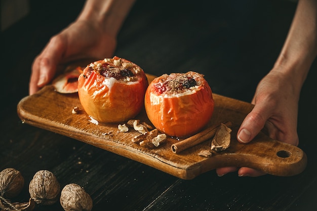 Pommes au four avec du fromage cottage avec des baies et des noix, garnies de miel et saupoudrées de cannelle. sur une surface en bois dans un style rustique