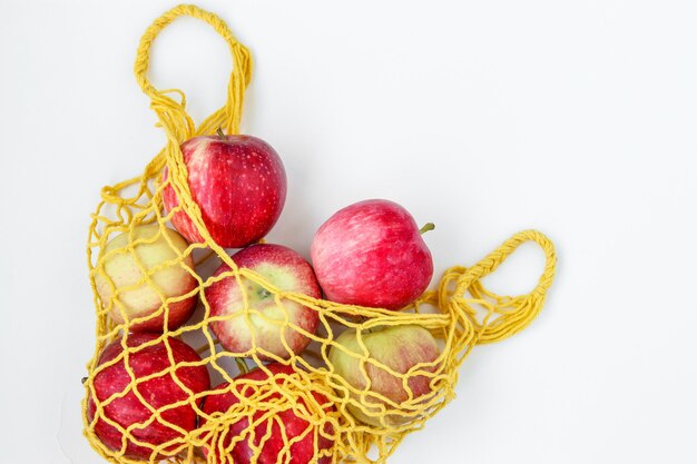 Pommes biologiques fraîches dans un sac textile jaune Shopping sur fond blanc, orientation horizontale, concept zéro déchet, espace copie