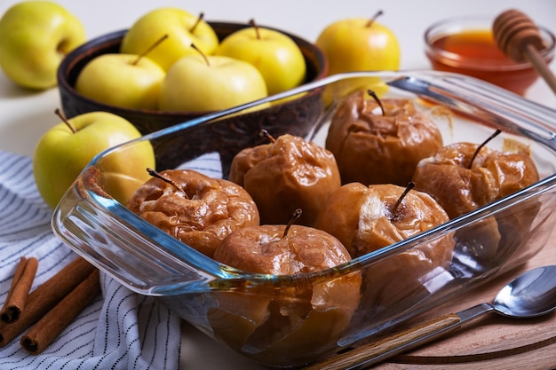 Photo des pommes caramélisées au four avec du miel dans un plat de cuisson réfractaire en verre sont placées sur la table parmi les pommes jaunes. mise au point sélective