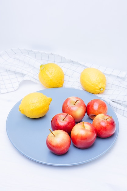 Pommes et citrons frais dans une assiette sur fond blanc.