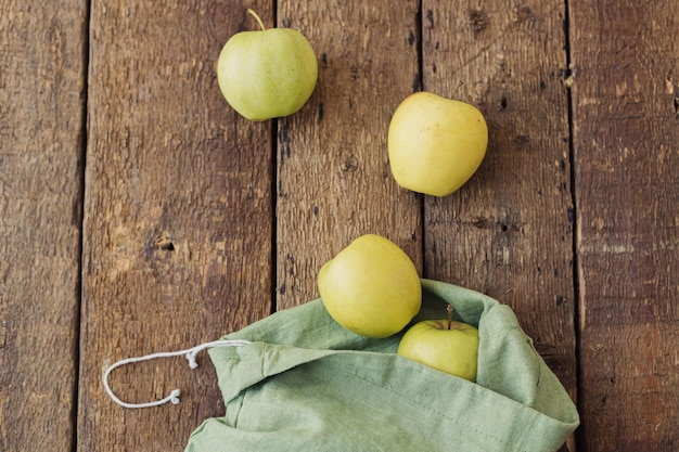 Pommes fraîches éparpillées dans un sac en coton écologique sur une vue de dessus en bois rustique Achats et livraison zéro déchet