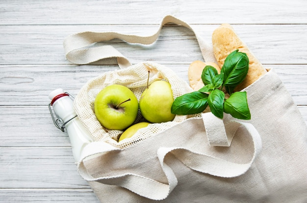 Pommes fraîches, lait et pain dans un sac en coton écologique sur une table en bois blanc