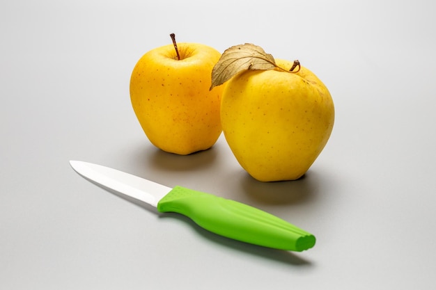 Pommes jaunes entières et un couteau sur fond gris Fruits biologiques