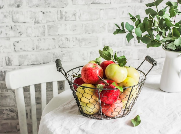 Pommes mûres fraîches dans un panier vintage en métal sur la table de la cuisine sur fond clair