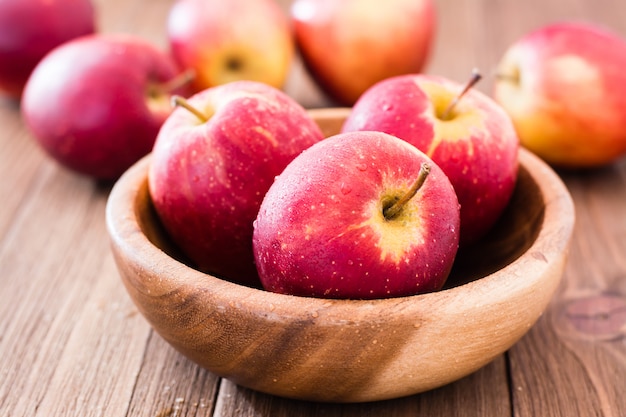 Pommes mûres rouges dans une assiette en bois et sur une table en bois