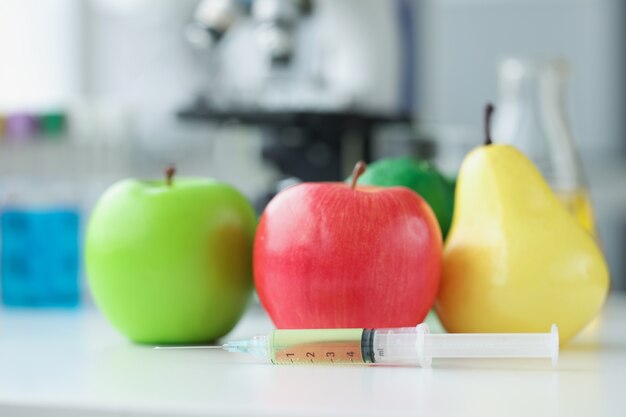 Pommes et poires allongées sur une table en laboratoire près d'une seringue avec un médicament en gros plan. Concept de production chimique de pesticides