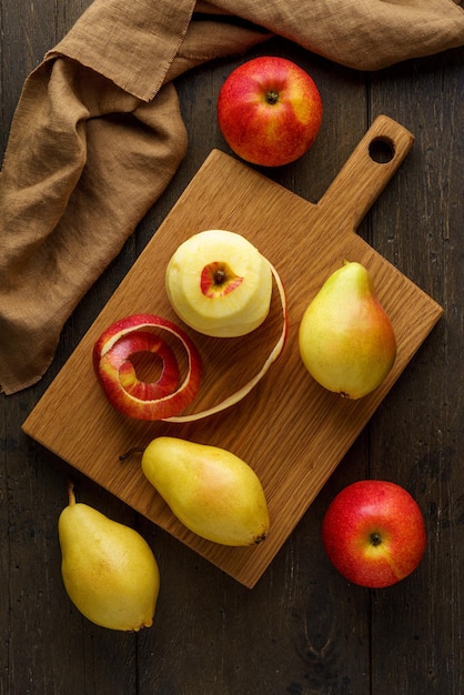 Pommes et poires rouges pelées sur une planche à découper en bois à la verticale de l'arrière-plan alimentaire