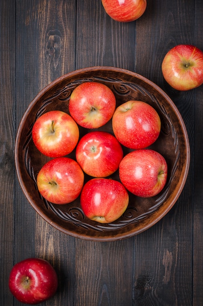 Pommes rouges sur un fond rustique foncé dans un bol en argile. Lay plat.