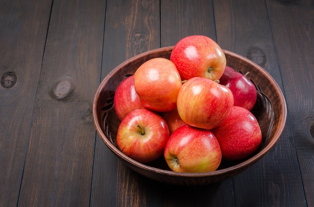 Pommes rouges sur un fond rustique foncé dans un bol en argile. Lay plat.