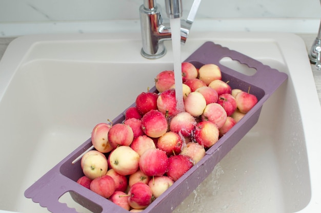 Pommes rouges fraîches dans l'évier de la cuisine, gros plan. Pommes dans une passoire, lavées à l'eau courante.