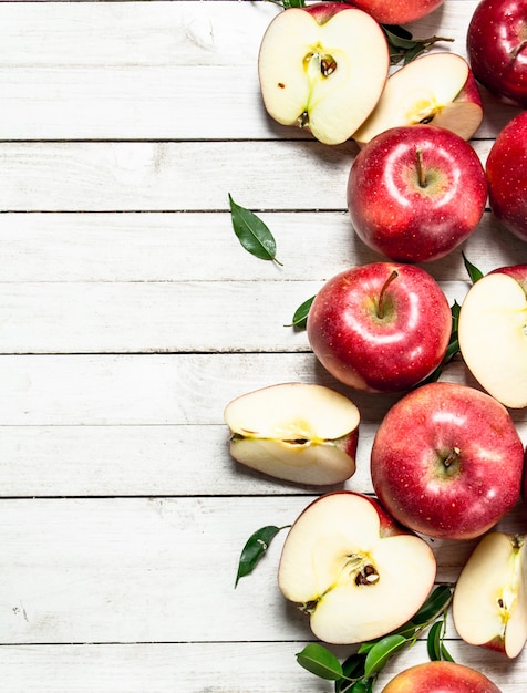 Pommes rouges fraîches avec des feuilles. Sur une table en bois blanche.