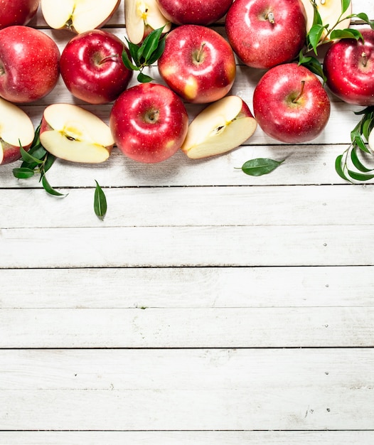 Pommes rouges fraîches avec des feuilles. Sur une table en bois blanche.