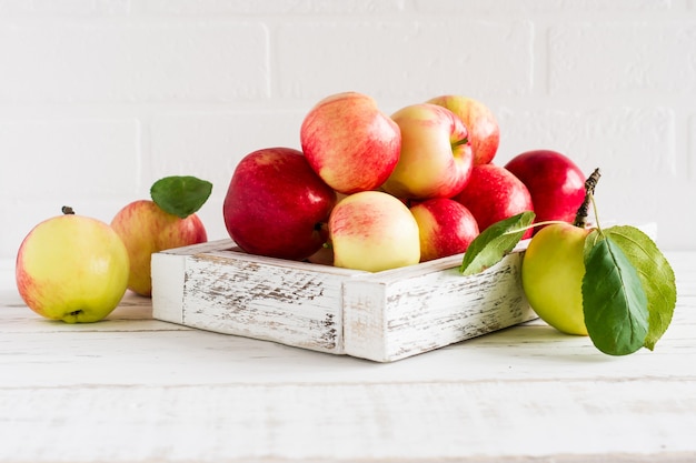 Pommes rouges et jaunes de saison dans une boîte décorative sur fond de mur de briques blanches.