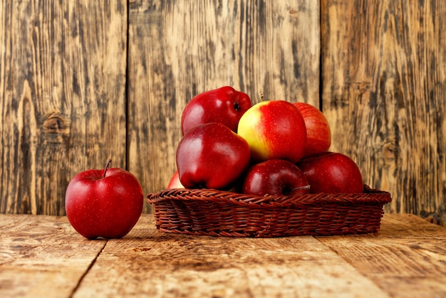 Photo des pommes rouges mûres dans un panier en osier sur une vieille table en bois