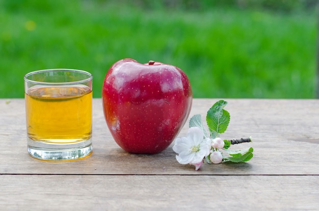 Pommes rouges et savoureuses avec un verre de cidre (jus de pomme) sur une table en bois