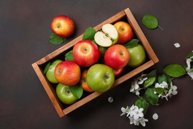 Pommes rouges et vertes mûres dans une boîte en bois avec branche de fleurs blanches sur fond rouillé. Vue de dessus avec un espace pour votre texte.