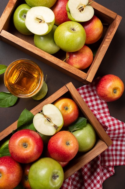 Pommes rouges et vertes mûres dans une boîte en bois avec un verre de jus de fruits frais sur fond rouillé. Vue de dessus.